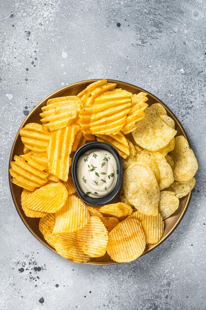 Variété de chips de pommes de terre dans une assiette servie avec sauce dip Fond gris Vue de dessus