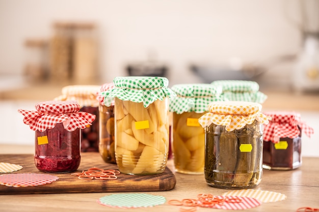 Variété de cornichons et de conserves faits maison, dessus à carreaux et étiquettes jaunes sur les pots.