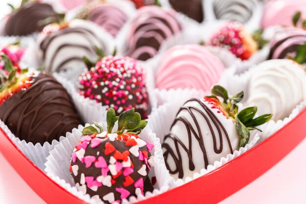 Variété de fraises enrobées de chocolat dans une boîte en forme de cœur.