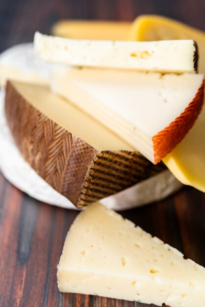 Variété de grandes tranches de fromage gastronomique sur un fond en bois foncé.