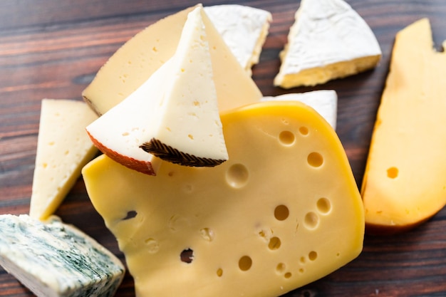 Variété de grands quartiers de fromage gastronomique sur fond de bois foncé.