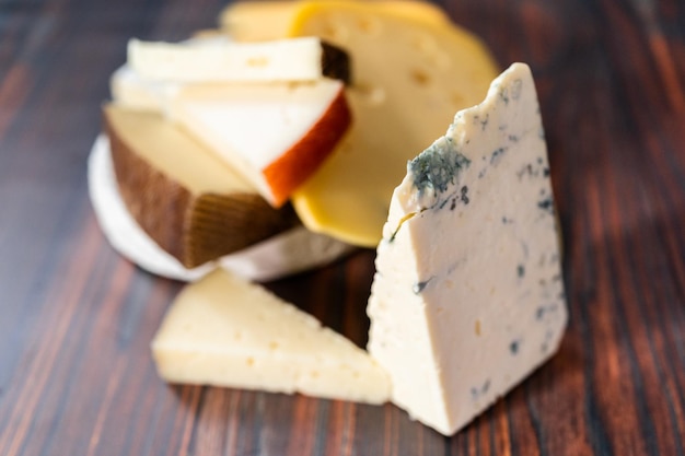 Variété de grands quartiers de fromage gastronomique sur fond de bois foncé.