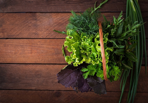 Variété d&#39;herbes organiques fraîches (laitue, rugule, aneth, menthe, laitue rouge et oignon) sur un fond en bois de style rustique.