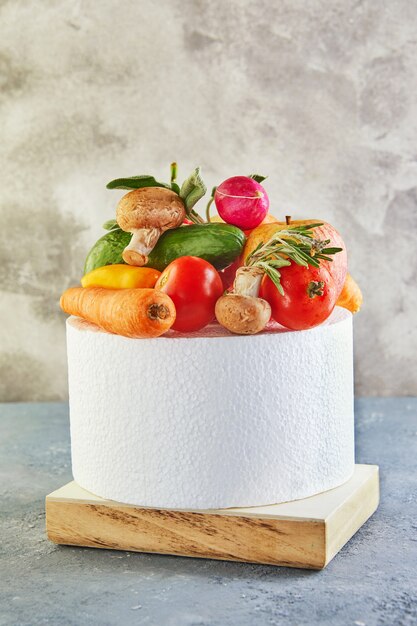 Une variété de légumes et de fruits allongé sur un podium blanc, sur un fond gris-bleu