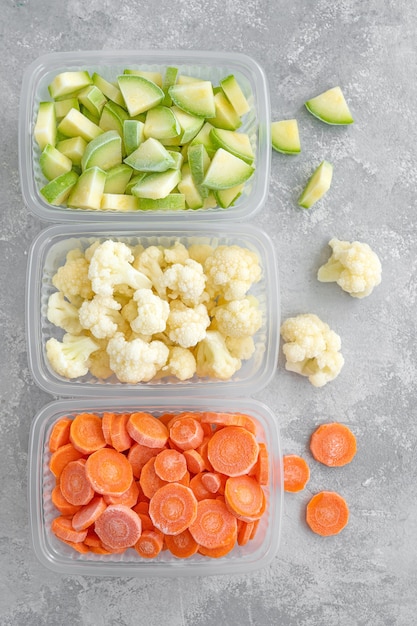 Une variété de légumes surgelés dans des récipients en plastique sur un fond de béton gris Copiez l'espace