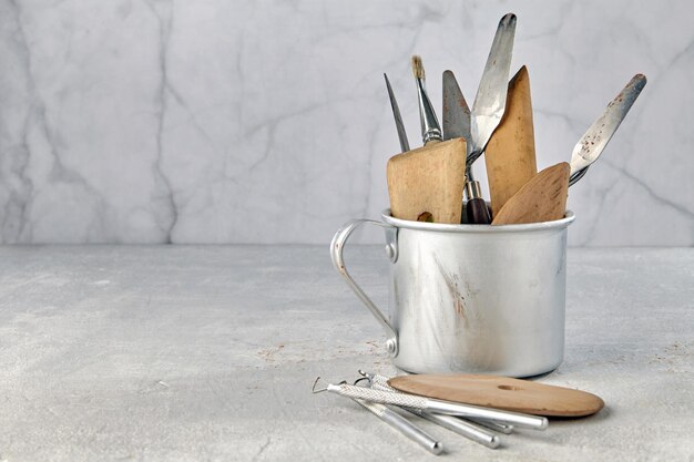 Variété d'outils pour sculpter et modeler dans une tasse en aluminium et sur un fond de pierre clair