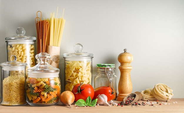 Variété de pâtes italiennes sèches dans des jarres de verre et des épices sur une table en bois