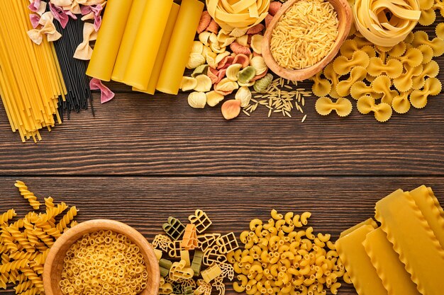 Variété de pâtes italiennes traditionnelles : spaghettis colorés, tagliatelles, farfalle, penne, ptititm, nouilles, fusilli, cannelloni sur un fond en bois ancien. Vue de dessus avec espace de copie.