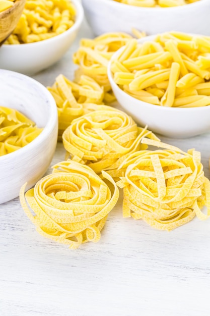 Variété de pâtes sèches jaunes dans de petits bols ronds.