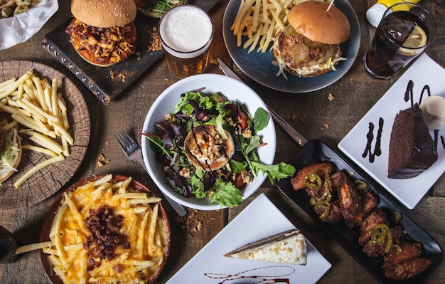 Photo variété de plats, hamburgers maison classiques salade de fromage de chèvre, frites et desserts sur table en bois. menu du menu du restaurant.