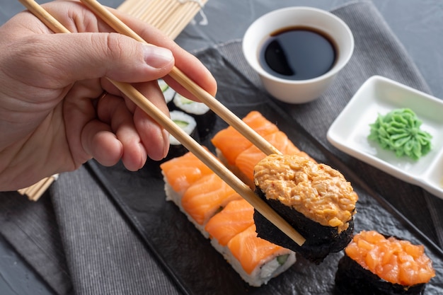 Une variété de rouleaux et de sushis japonais sur une plaque noire texturée. Vue de côté. Les bâtons de bambou contiennent un gunkan. Fermer