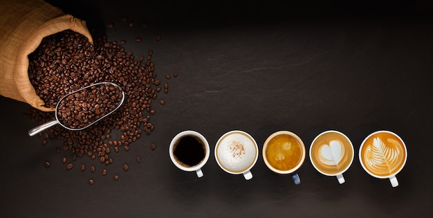 Photo variété de tasses de café et de grains de café dans un sac de jute sur fond noir