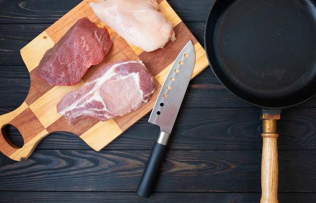 Variété de viande de boeuf crue sur os, viande de porc et filet de poulet sur table en bois avec couteau de boucher, vue de dessus