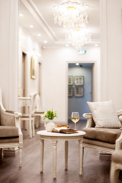 Un vase avec de belles fleurs blanches, un verre de vin et des pâtisseries croquantes se dressent sur la table dans une pièce lumineuse et confortable. Tournage à l'intérieur