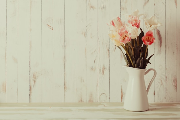 Vase blanc aux nuances délicates brassée de tulipes sur fond de bois