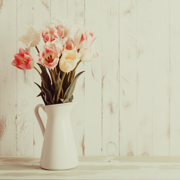 Vase blanc aux nuances délicates brassée de tulipes sur fond de bois