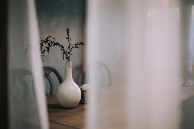 Vase blanc avec branche sèche se dresse sur une table en bois. Le design minimaliste de la pièce.