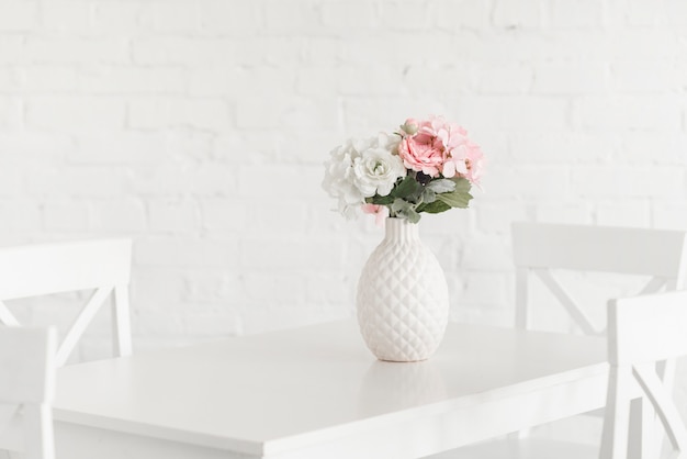 Vase blanc fleurissant sur la table contre le mur de briques