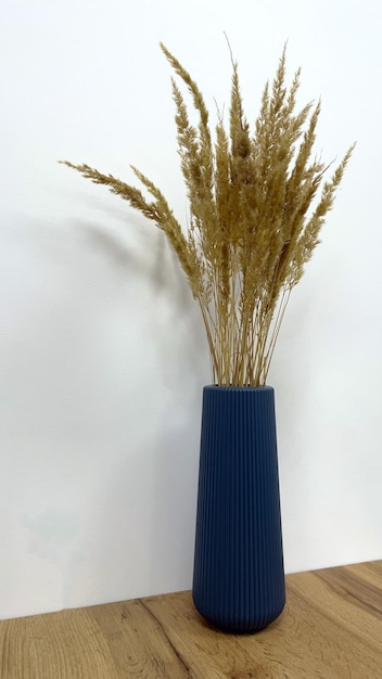 Photo vase bleu moderne élégant sur une table en bois avec un bouquet de fleurs séchées contre un mur blanc