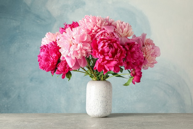 Vase avec bouquet de belles pivoines sur table grise sur fond bleu