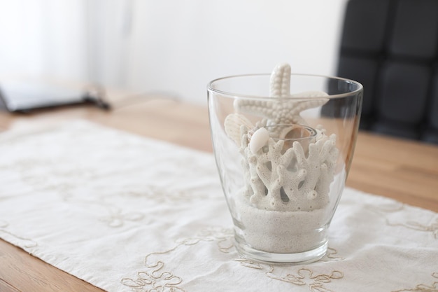 Un vase avec du sable blanc et des coquillages et des étoiles de mer sur une table ambiance vacances