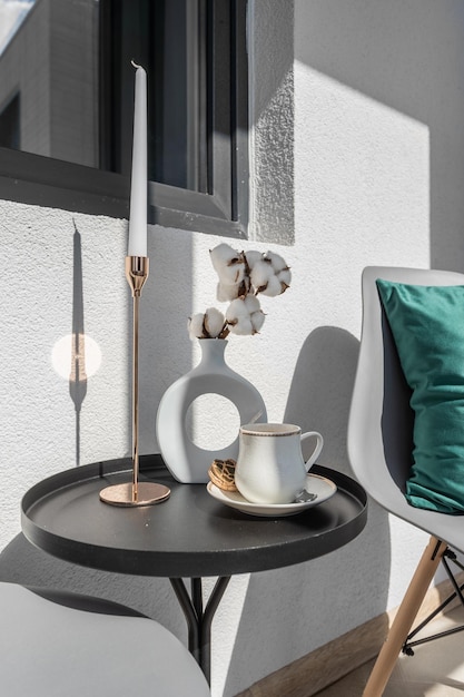 Un vase avec des fleurs de coton une bougie dans un chandelier et une tasse de café sur une table