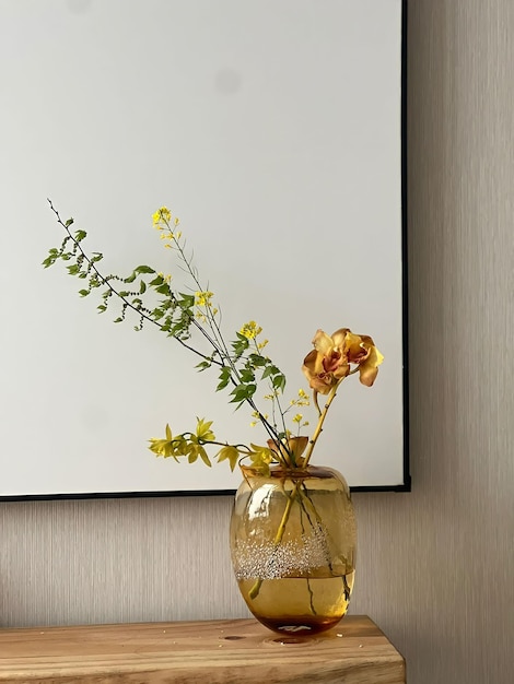 Un vase de fleurs est posé sur une table avec un cadre noir derrière.