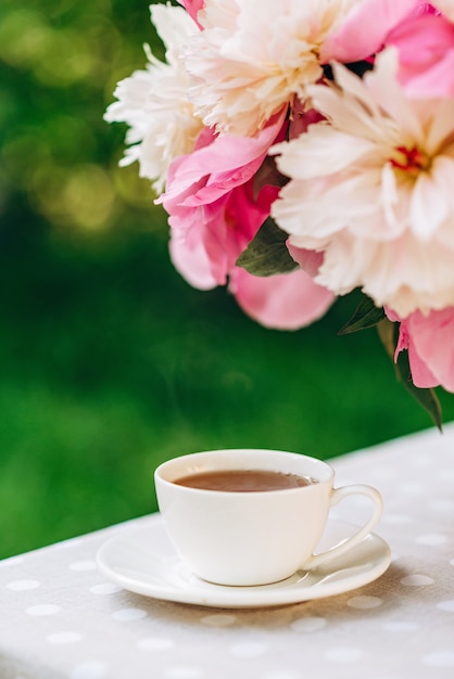 Un vase de fleurs de pivoines près d'une tasse de café