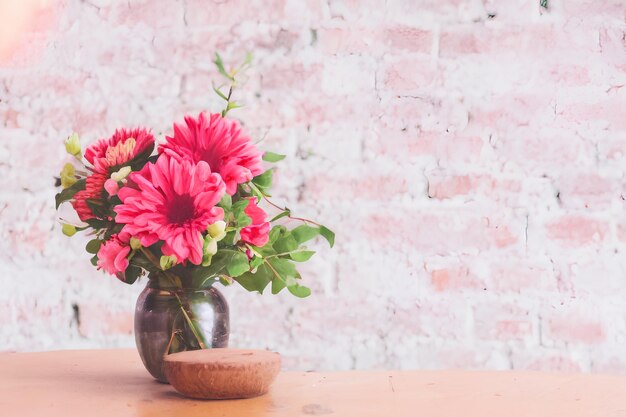 Un vase de fleurs sur une table avec un mur de briques derrière