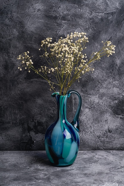 Vase pichet bleu avec gypsophile en vrac fleurs blanches séchées sur fond de pierre texturée sombre, vue d'angle