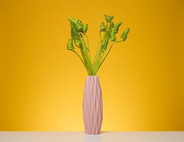 Vase rose avec des fleurs séchées vertes sur un tableau blanc fond jaune