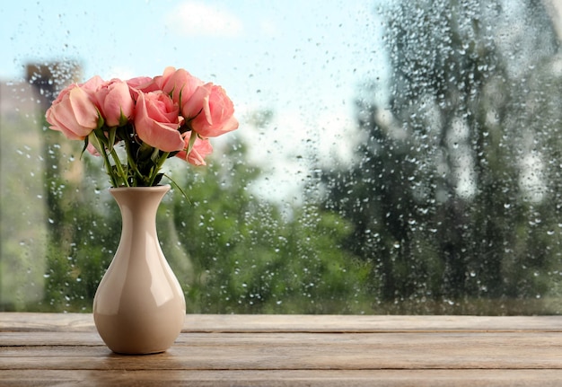 Vase avec des roses près de la fenêtre le jour de pluie Espace pour le texte