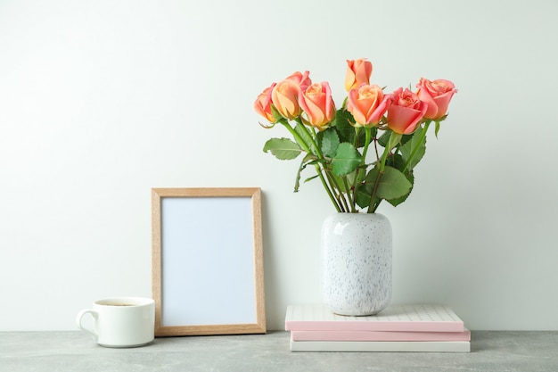 Photo vase avec roses roses, cahiers, cadre vide, tasse de café sur la table grise