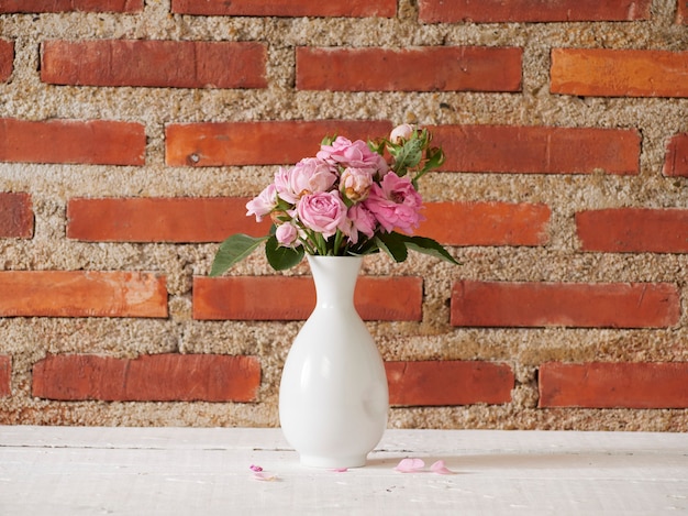 Vase avec des roses roses sur table blanche près du mur de briques