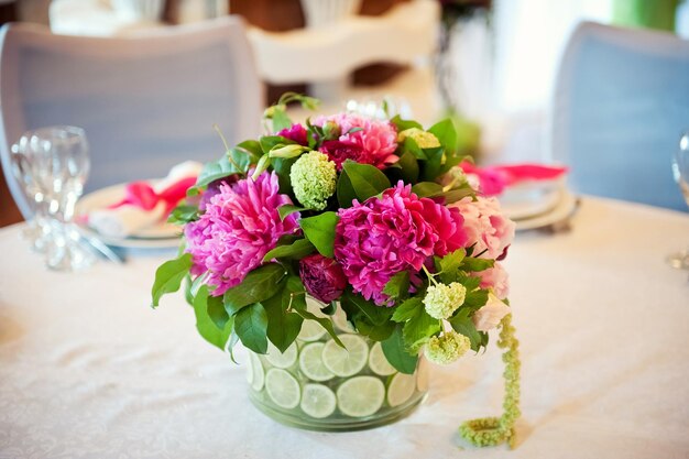 Vase transparent de décoration de table de mariage avec des tranches de pivoines roses d'agrumes contre la nappe blanche