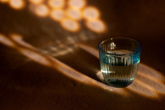 Vase en verre bleu sculpté avec de l'eau sur fond sable avec lumière et ombre et espace de copie