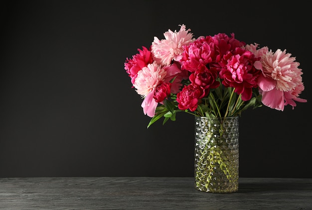 Vase en verre avec bouquet de belles pivoines sur table en bois sur fond noir