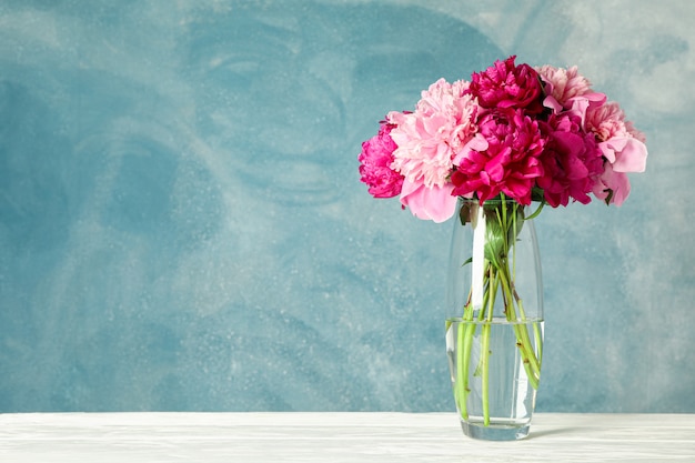 Vase en verre avec bouquet de belles pivoines sur tableau blanc sur fond bleu