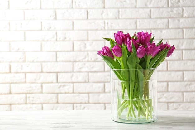 Vase en verre avec bouquet de belles tulipes sur fond de mur de briques