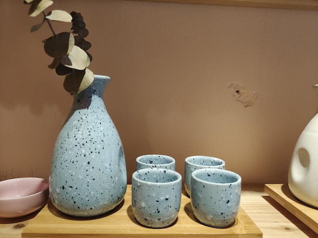 Un vase et des verres sont sur une table avec un mur rose derrière eux.