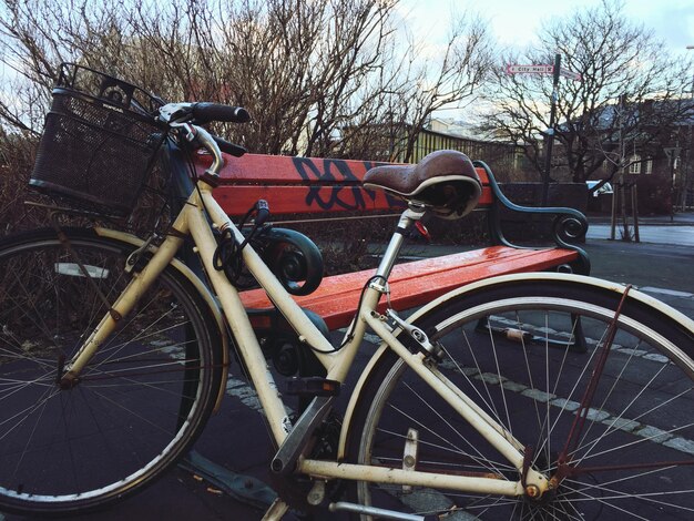 Photo vélo garée par un banc sur le trottoir contre des arbres nus