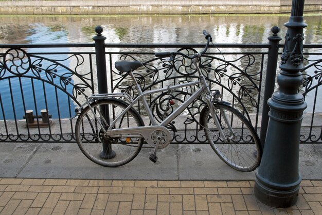 Vélo gris garé près d'un lampadaire et enchaîné à la balustrade du remblai du bord de la rivière carrelé jaune