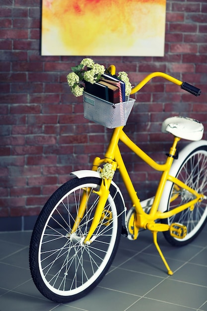 Vélo jaune avec des livres sur fond de mur de briques