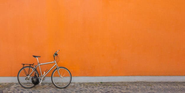 Photo un vélo noir garé à côté d'un mur orange en béton.