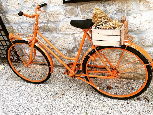 Vélo orange garé sur des gravier contre un mur de pierre