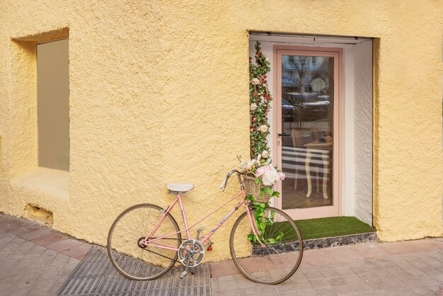 Vélo rose garé sur le mur d'un magasin jaune avec des fleurs