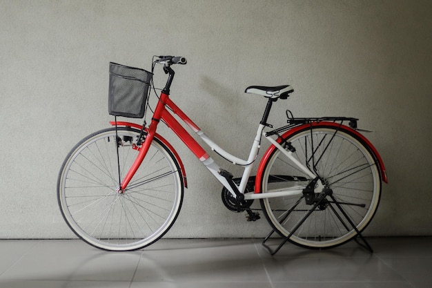 Vélo rouge avec panier devant un mur gris