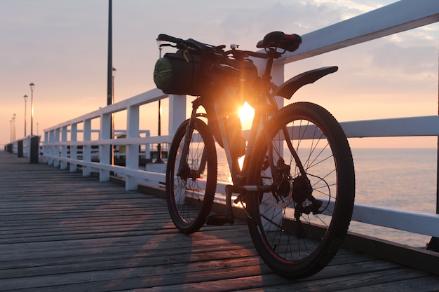 Vélo Avec Sacs Est Sur Le Quai Au Bord De La Mer, Au Lever Du Soleil