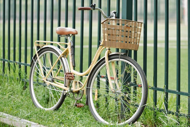 Un vélo vintage debout sur l'herbe près de la clôture Un vélo rétro jaune avec un panier en osier