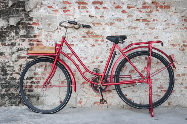 Vélo vintage rouge garé devant le mur de briques